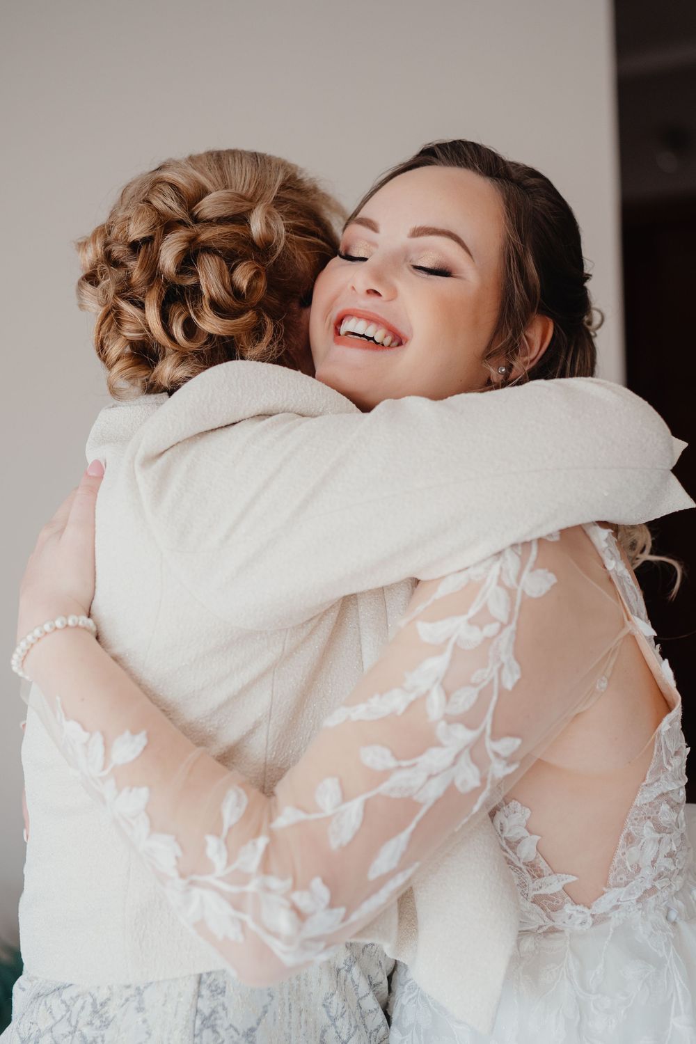 Two people wearing elegant white gowns share a joyful embrace during what appears to be a wedding celebration.