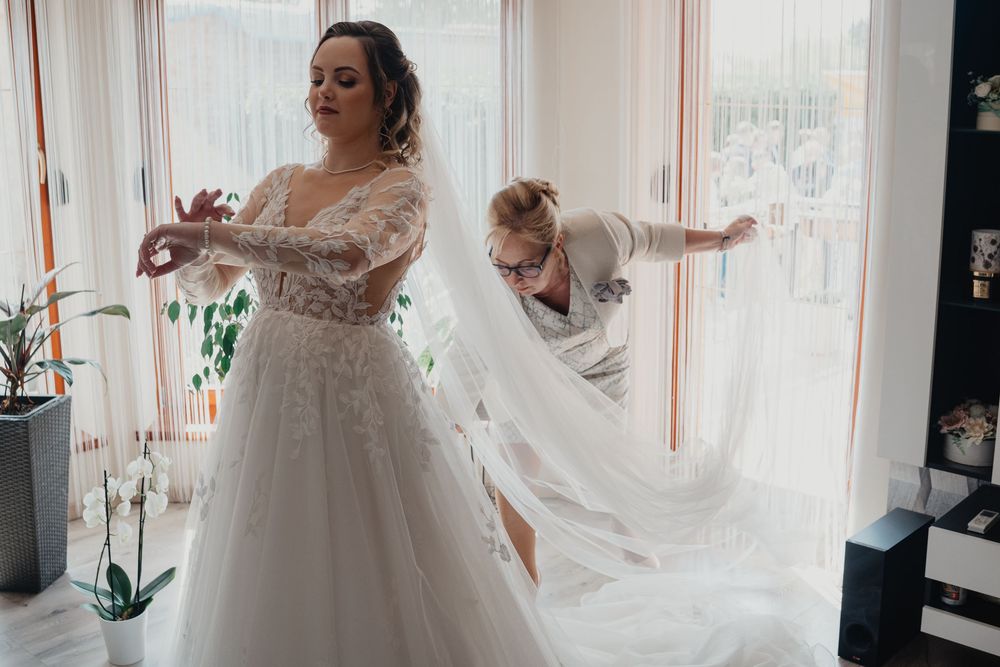 Behind the scenes bridal preparations showing beautiful flowing wedding dress and long white veil in bright room.