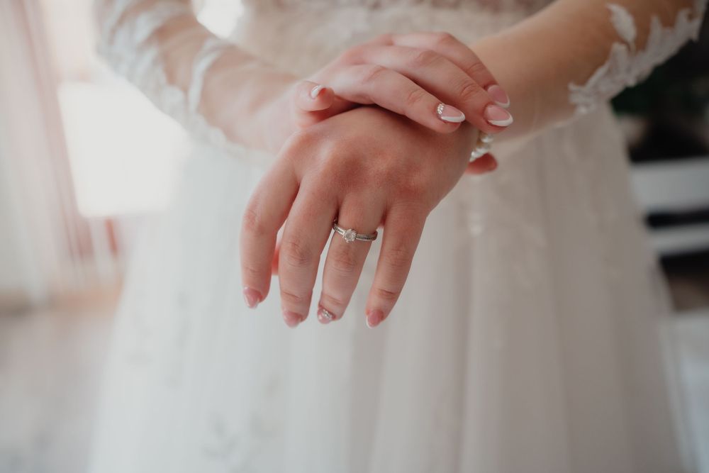 Hand wearing a sparkling diamond engagement ring shown against delicate white wedding dress fabric.