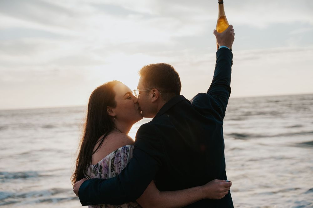 A couple shares a romantic moment at sunset on the beach while holding a bottle.
