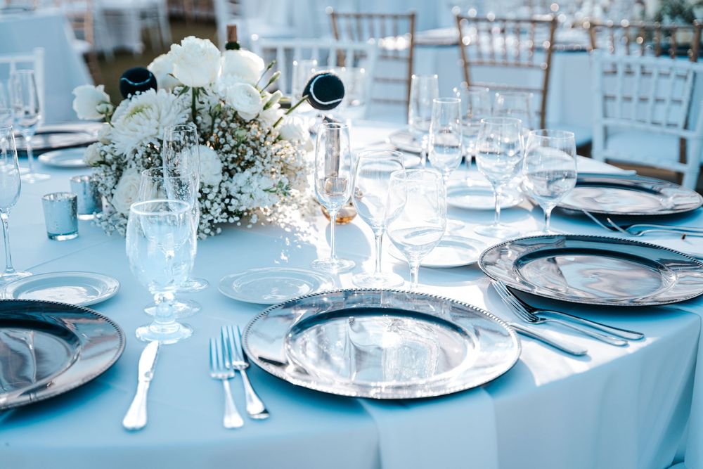 An elegant wedding table setting with light blue linens, white floral centerpiece and silver place settings.