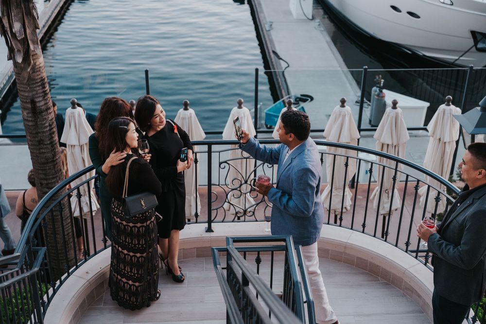 A small group gathers on a curved balcony overlooking boats and water at dusk.