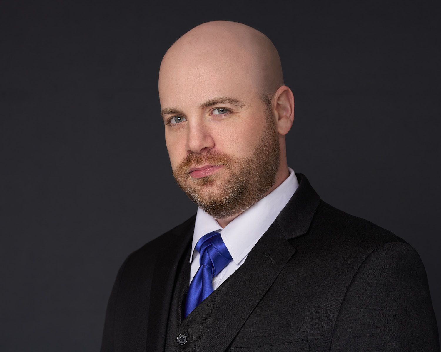 Bald-man-with-trim-beard-and-moustache-in-black-vest-suit-white-shirt-and-blue-tie