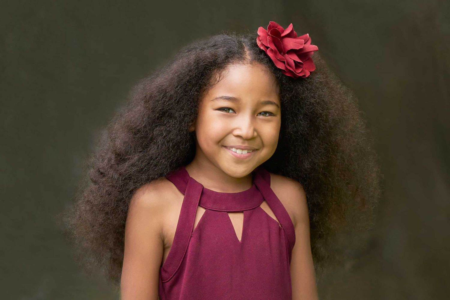 Asian-African American young girl with sweet smile and cranberry flower in her long dark hair