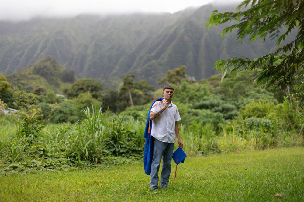 A person walks along a lush green path with dramatic mountain peaks shrouded in mist in the background in Hawaii.