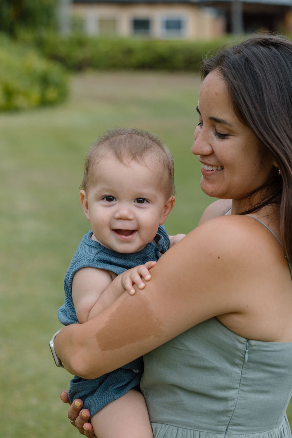 Mother holding smiling baby outdoors in a garden setting.