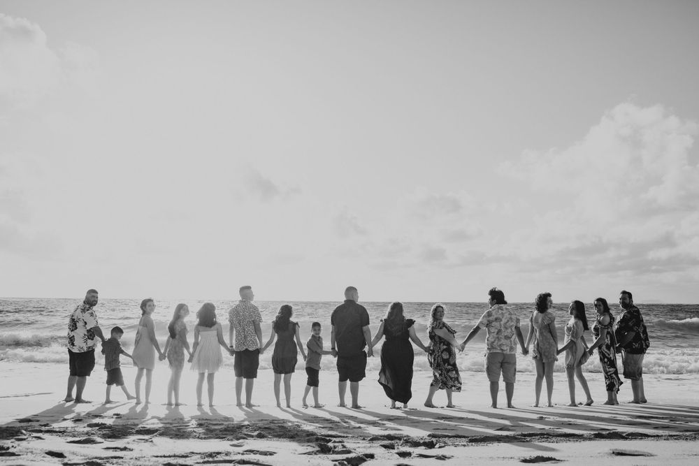 Large group holding hands in a line on the beach in black and white photography.