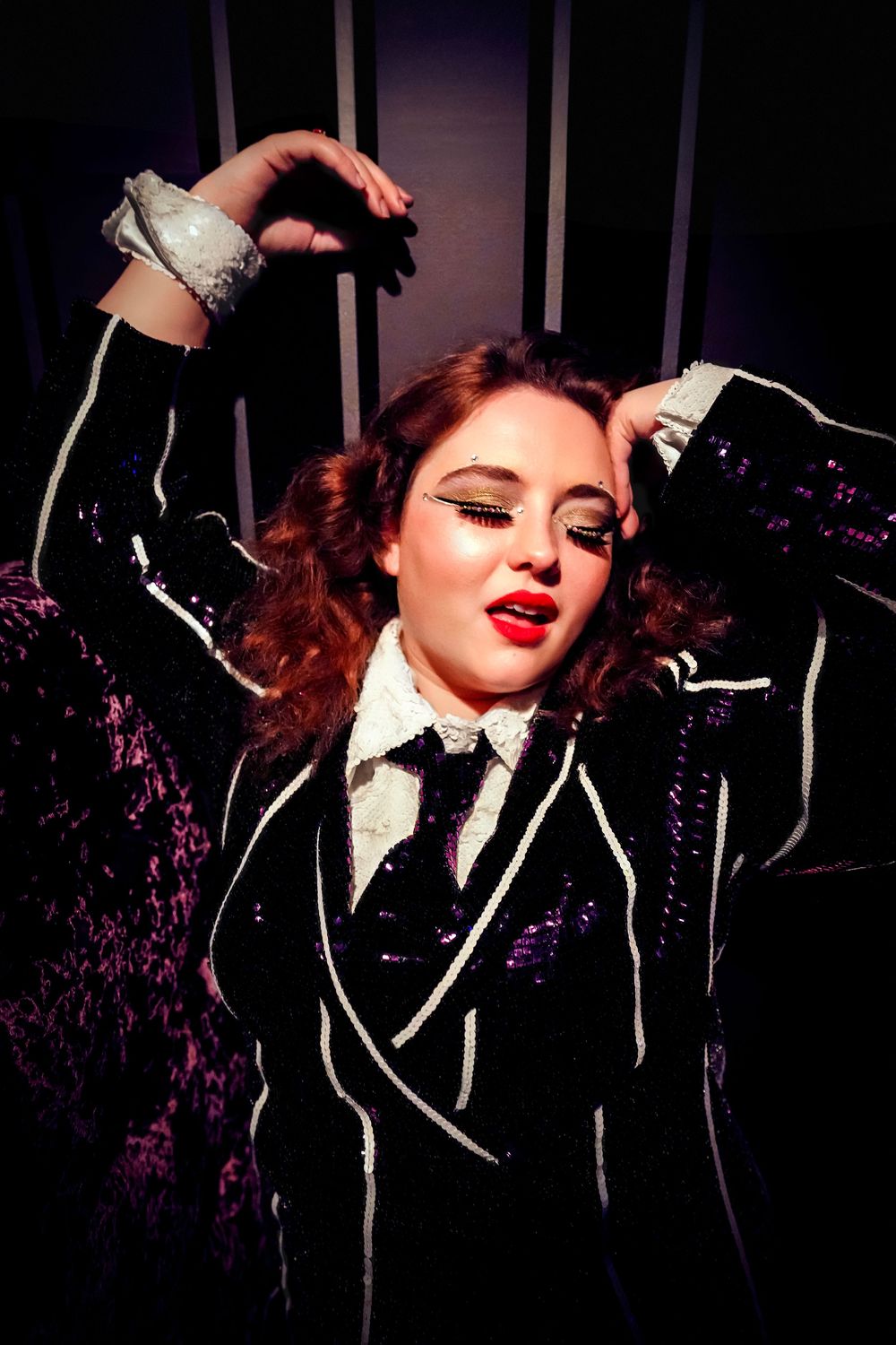 A glamorous vintage-inspired cabaret performance with red lipstick, sequined jacket and bow tie against a dark backdrop.
