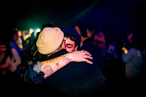 Two people embracing at nightclub with colorful lighting and crowd in background.