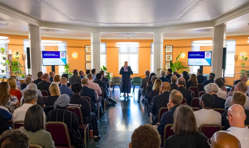Large audience gathered in a bright conference room with orange walls and modern presentation screens. corporate event
