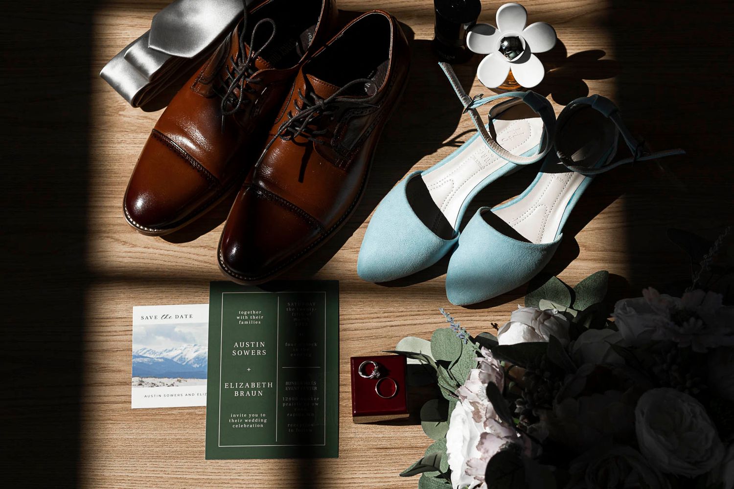 Wedding accessories including dress shoes, a green passport and other items arranged on wooden flooring.