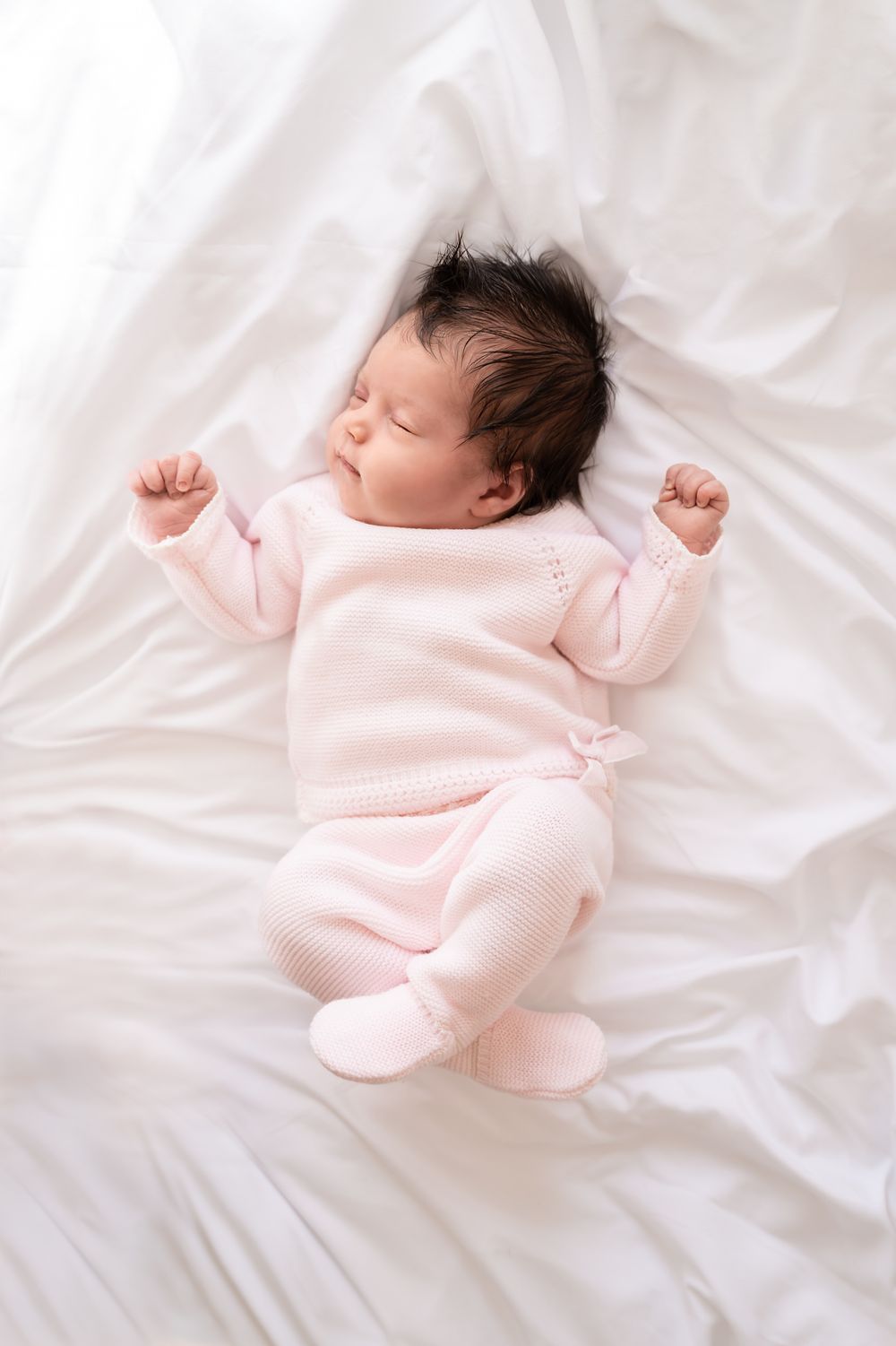 newbornshoot van een pasgeboren baby, vastgelegd in zachte tinten. in een huiselijke sfeer. baby op wit laken en roze kleding.