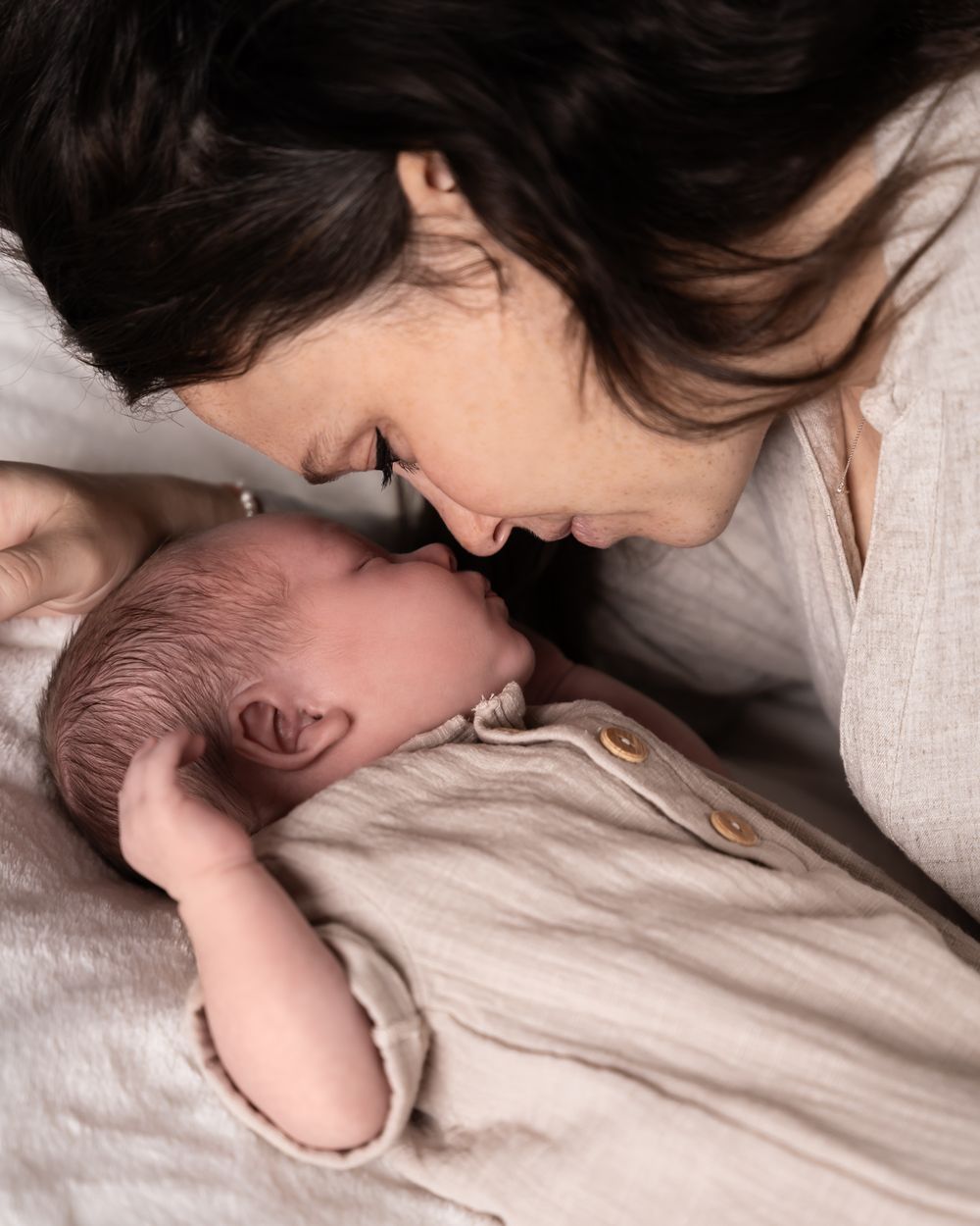 Een serene en liefdevolle close-up van moeder en pasgeboren baby, vastgelegd in zachte tinten en een warme sfeer gefotografeerd in maas&waal