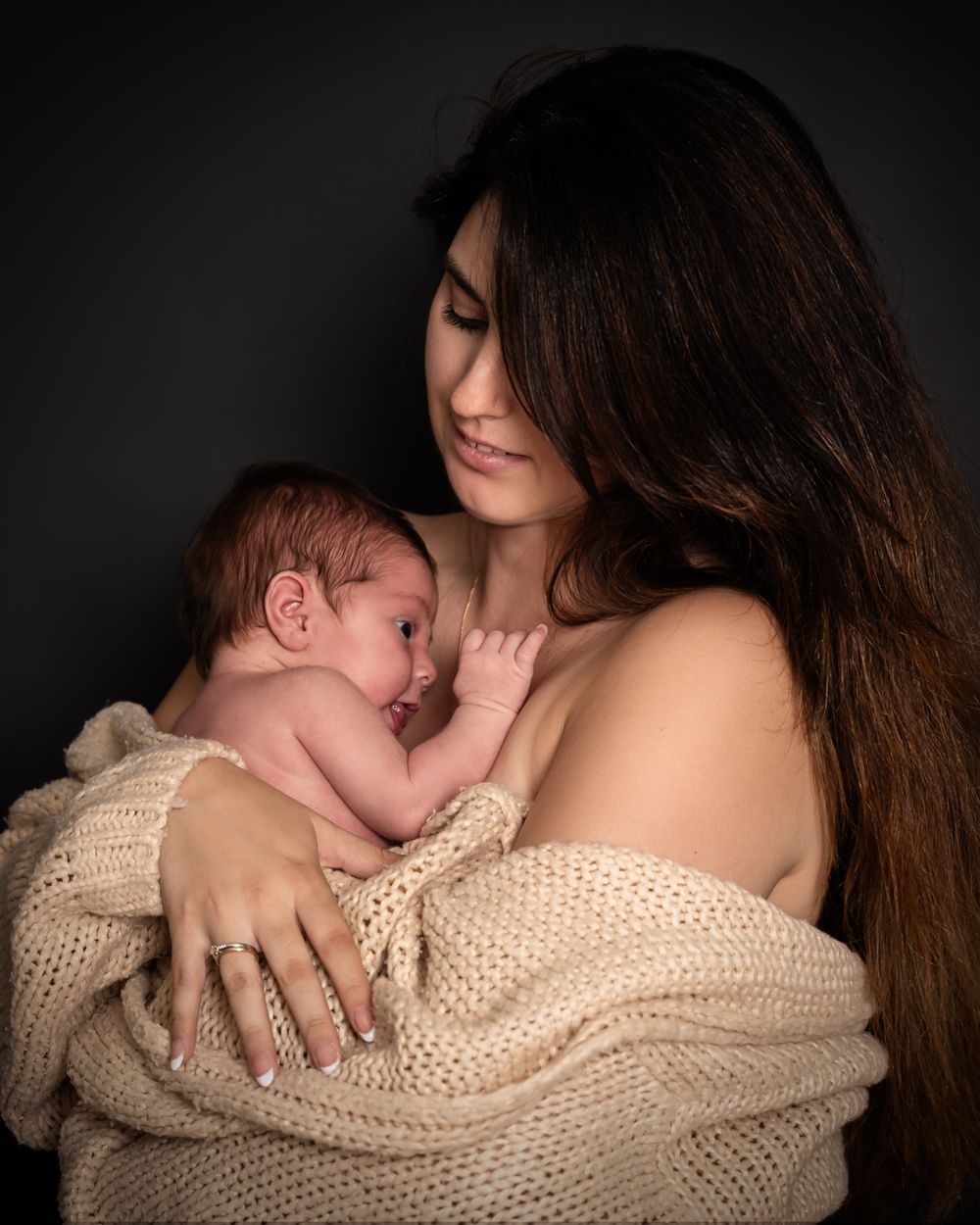 newbornshoot in studio in beneden-leeuwen, vrouw houdt pasgeboren baby vast, gewikkeld in beige doek.