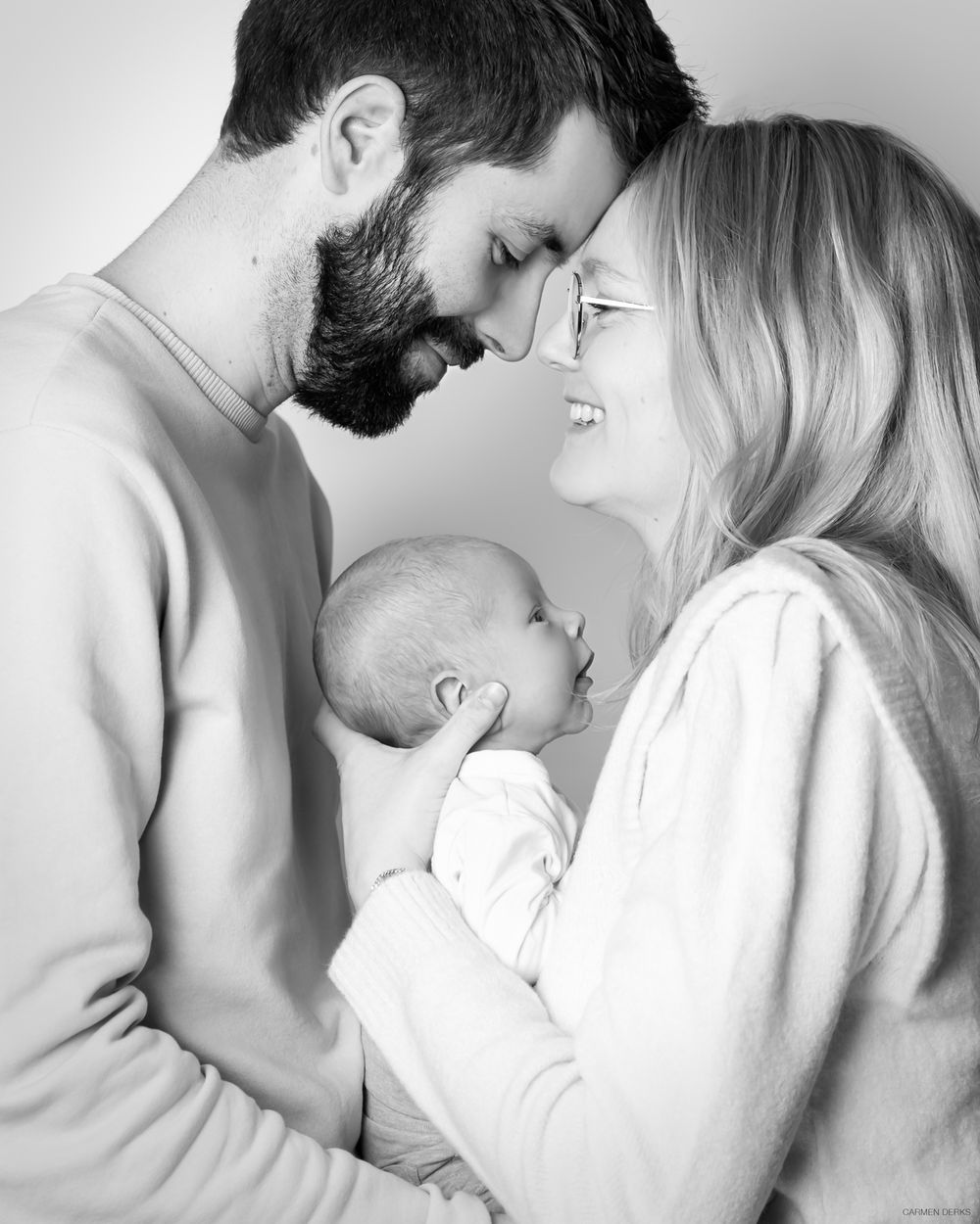 newbornshoot in studio. moeder houdt pasgeboren baby vast, vader en moeder kijken liefdevol naar elkaar gefotografeerd in maas&waal