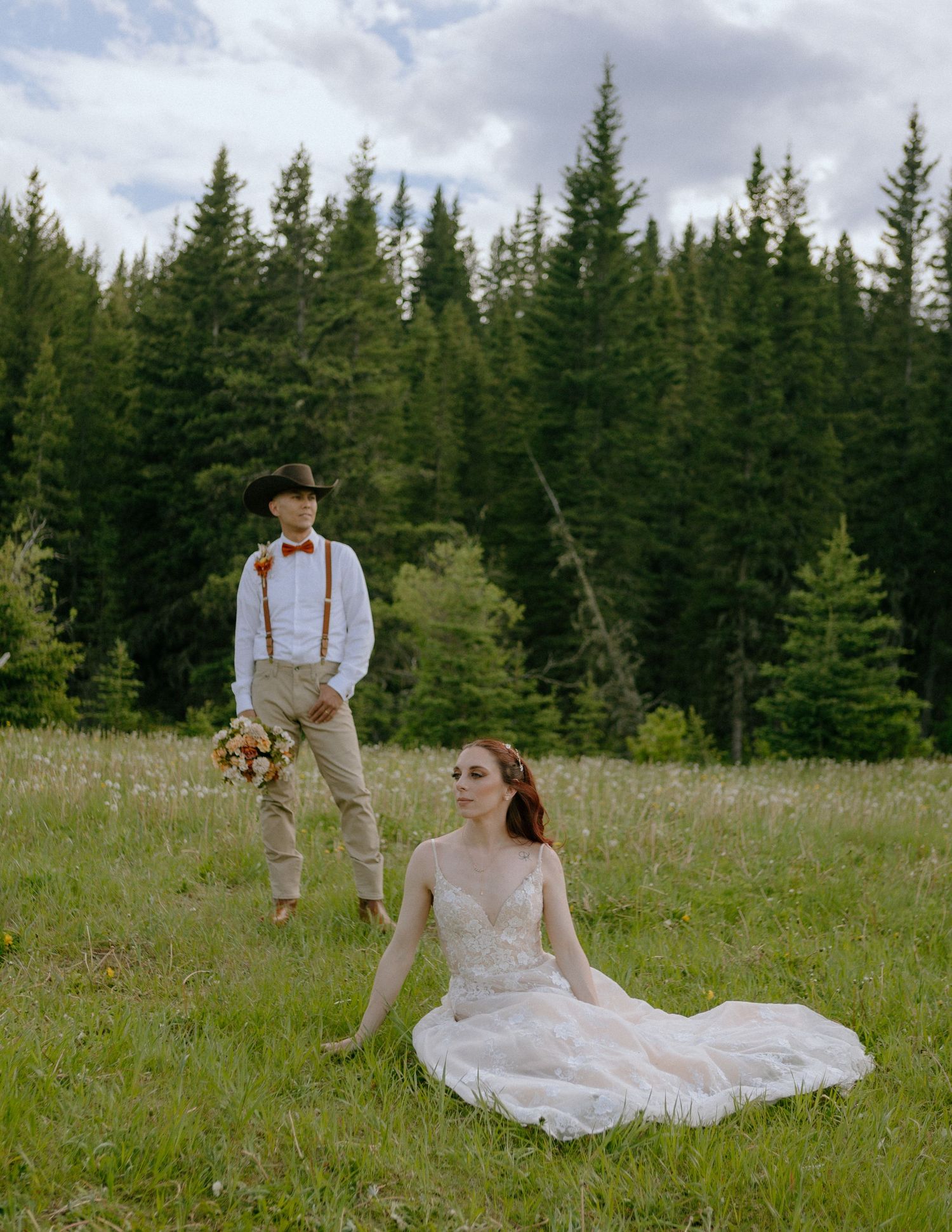 A rustic wedding portrait in a mountain meadow with tall pine trees in the background.