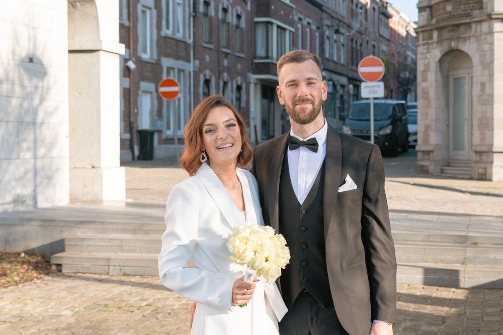Couple de mariés devant la maison communale de Huy au soleil, la mariée en blanc avec un bouquet jaune juste avant le mariage civil
