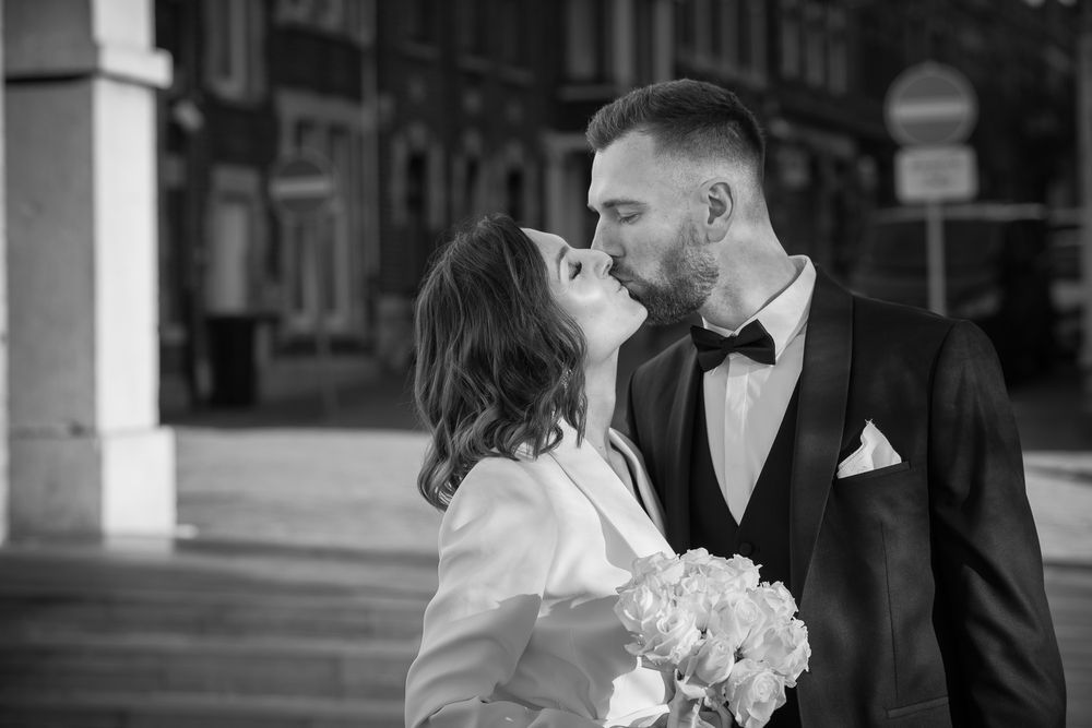 Mariés devant la maison communale, prêts à se dire oui, échangeant un baiser tout en tenant un bouquet de fleurs blanches