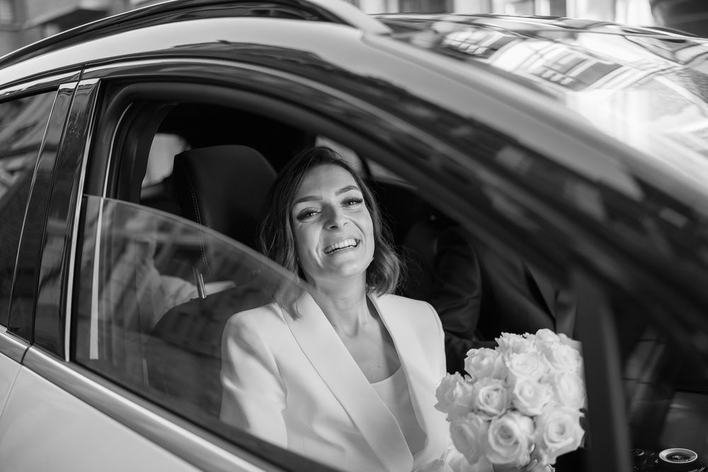 Mariée souriante en la voiture après le mariage à la maison communale de Huy, tenant un bouquet de roses, en route pour la Ferme de hepsée