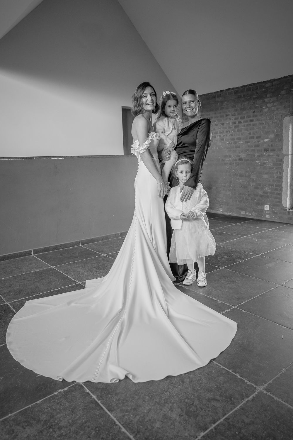 Mariée en noir et blanc à la Ferme d'Hepseé, posant élégamment sur un sol carrelé avec des invités en tenue formelle