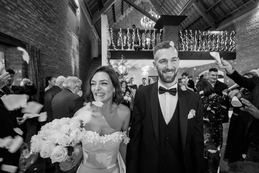 Photo en noir et blanc d'un couple riant lors de leur réception à la Ferme de Hepsée, entouré d'invités