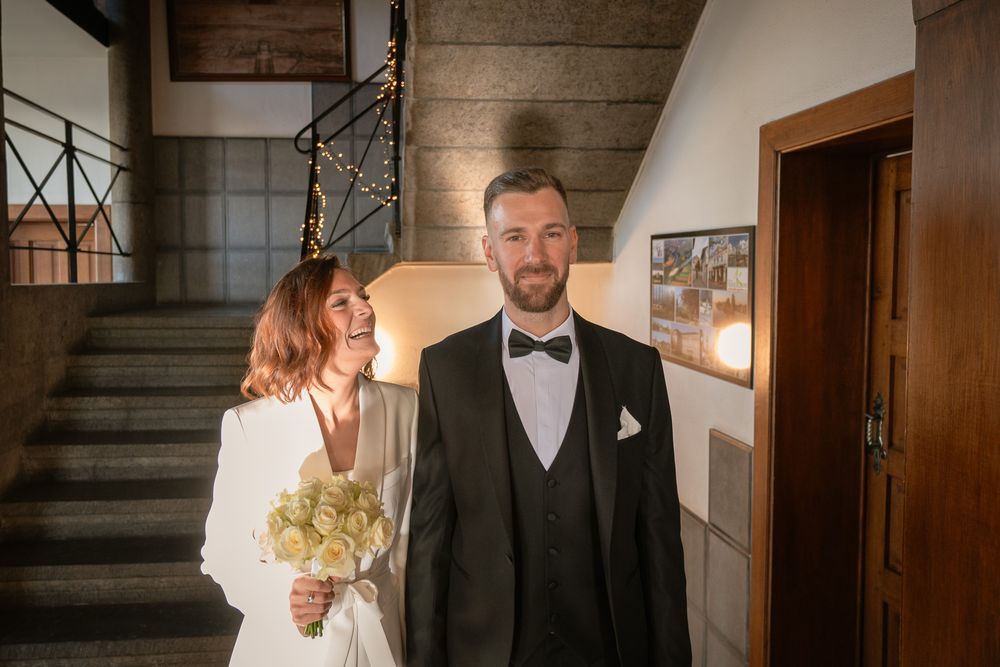 Mariés entrant dans la salle communale, la mariée tenant un bouquet blanc et doré dans un escalier