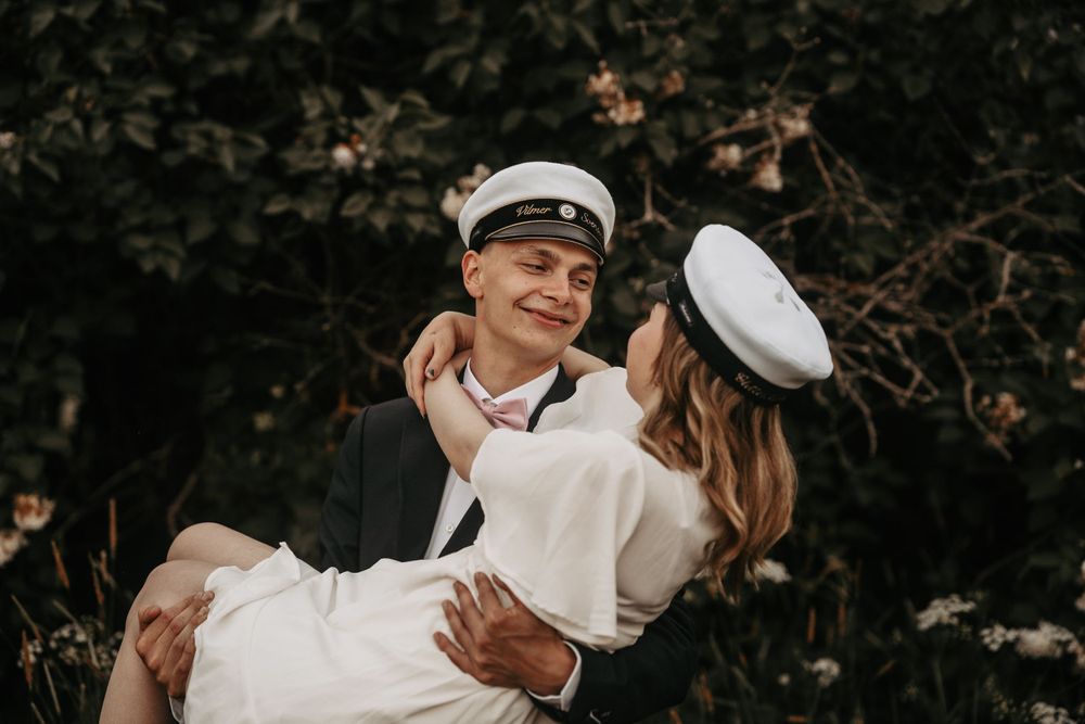Playful nautical themed couple portrait with white graduation caps in garden setting.