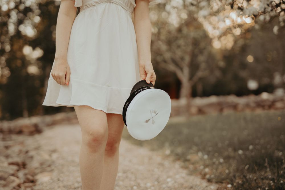 Figure in a white summer dress holding a vintage hat box in soft afternoon light.