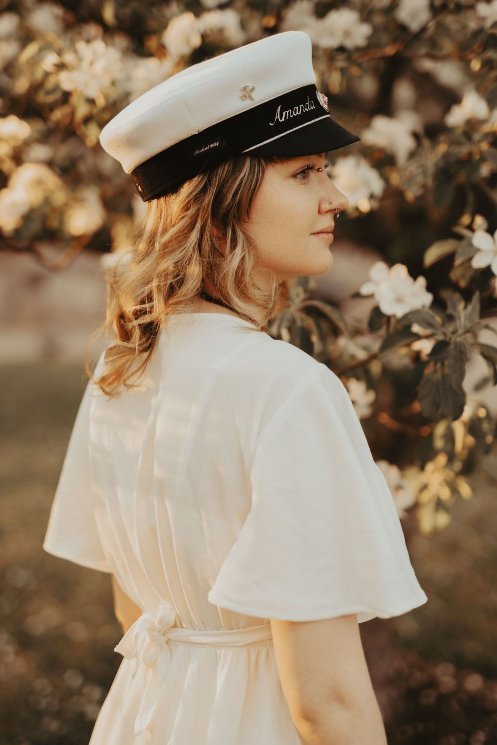 A dreamy portrait showing a white sailor cap and floral surroundings in warm golden light.