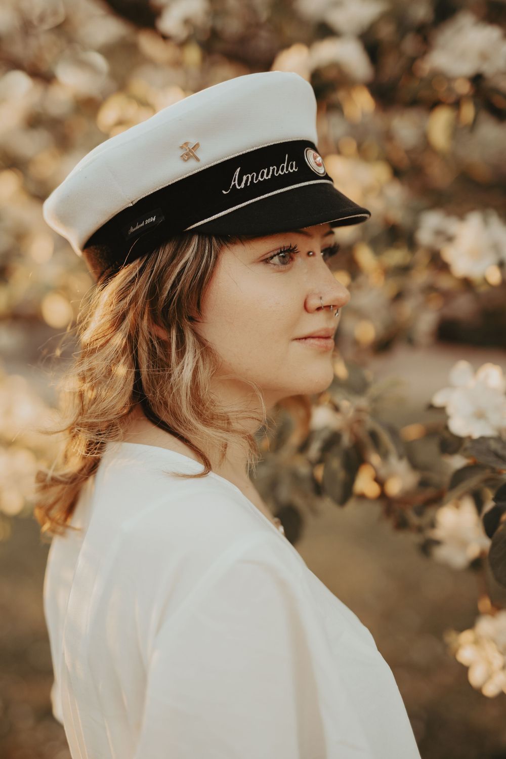 Side profile view of someone wearing a white nautical cap and dress against blooming spring flowers.
