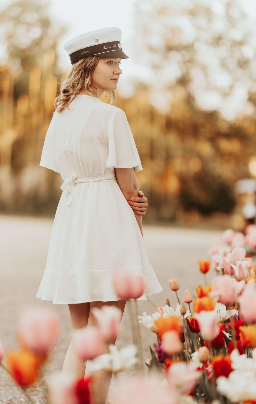 Person in white dress and sailor cap posed among colorful spring tulips at sunset.