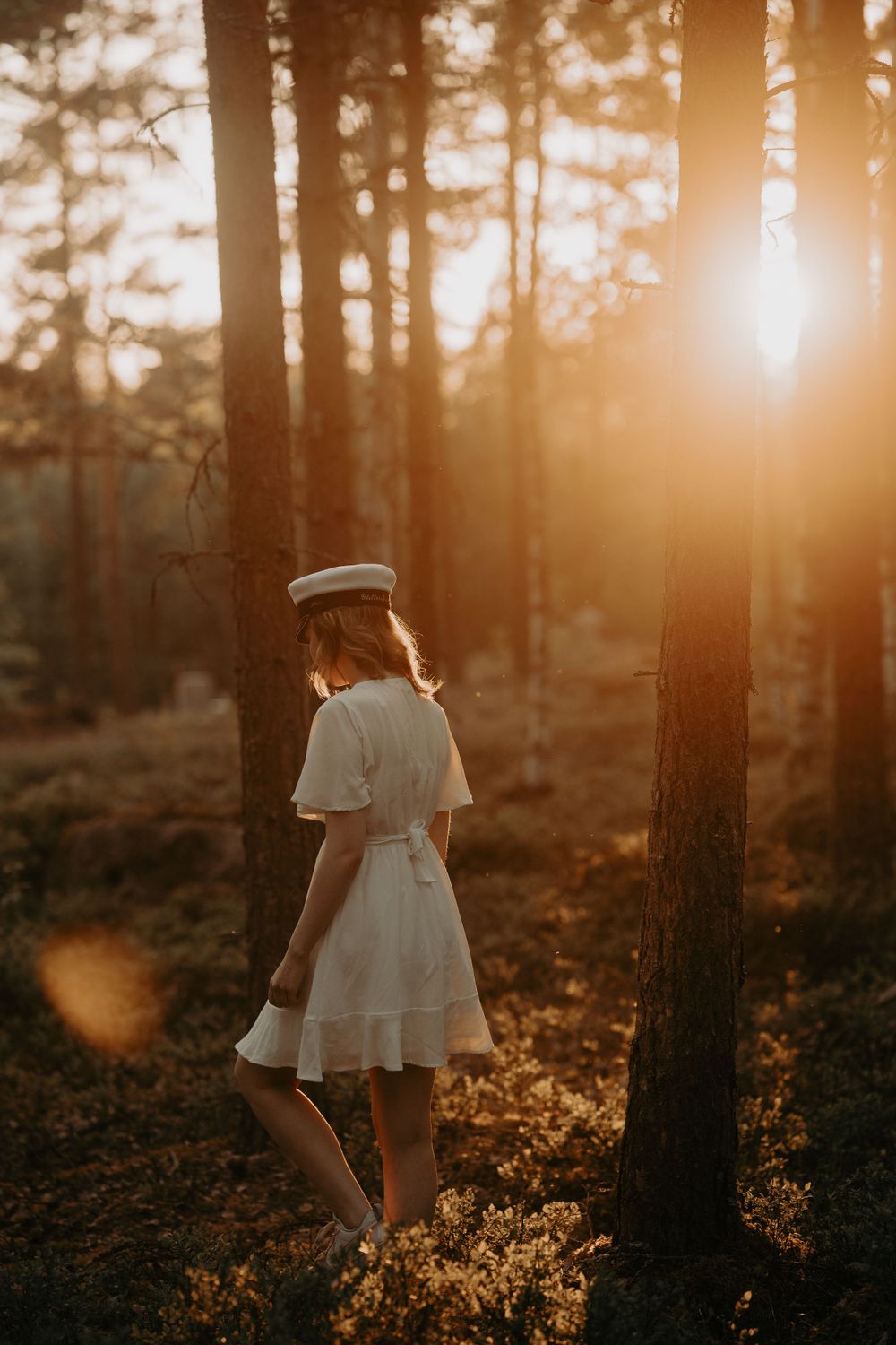 Ethereal forest scene with sunlight streaming through trees as figure stands in white dress.