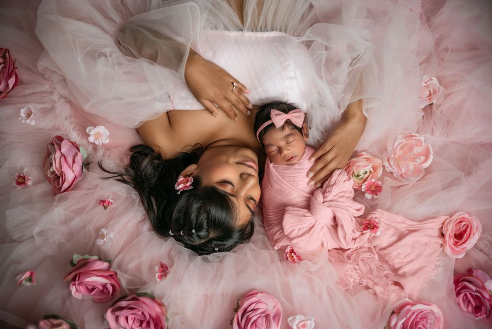 Overhead view of mother and baby lying among pink roses and tulle fabric.