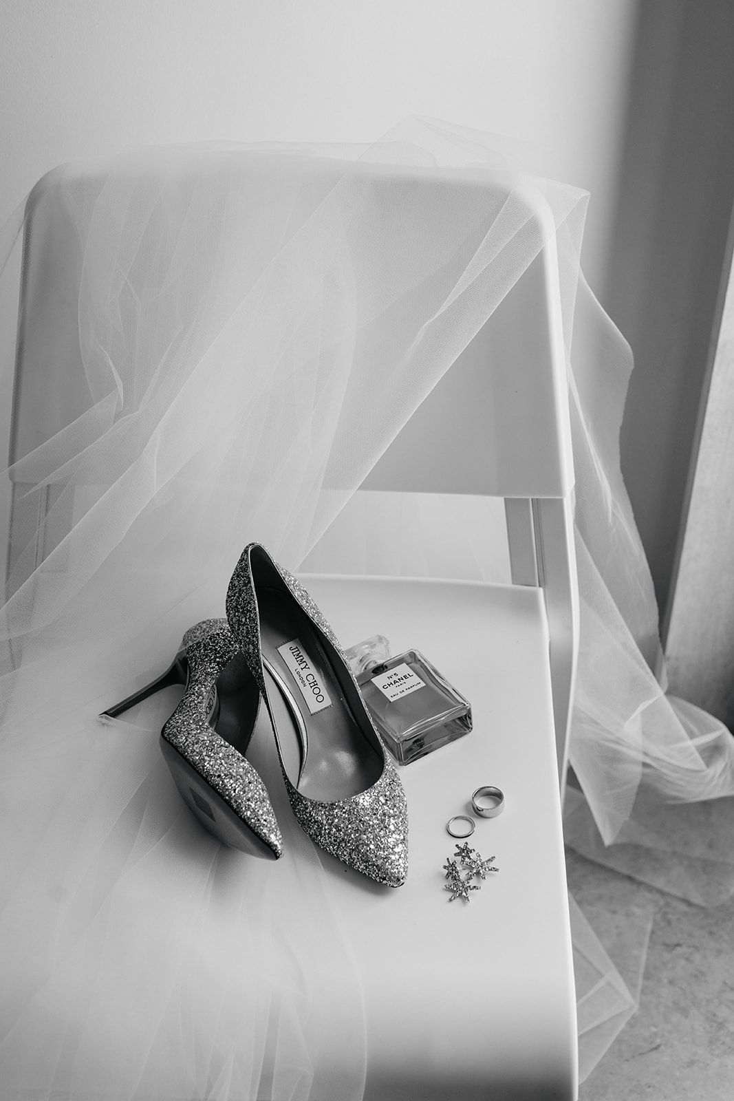 Sparkly silver wedding shoes and accessories styled with a flowing veil on white surface.