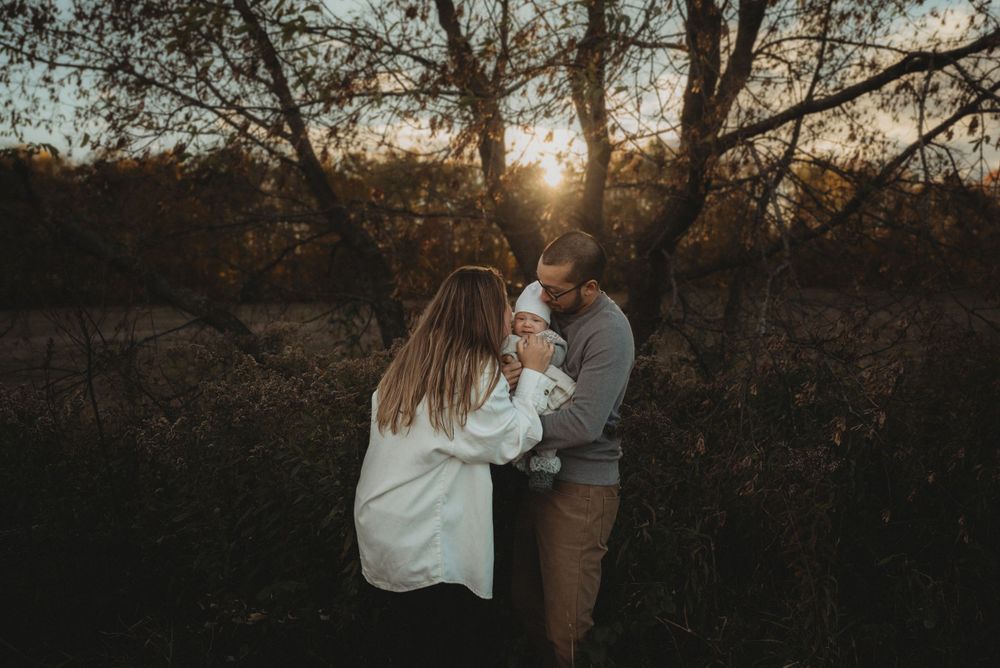 Tender family moment captured in golden sunset light among autumn trees.