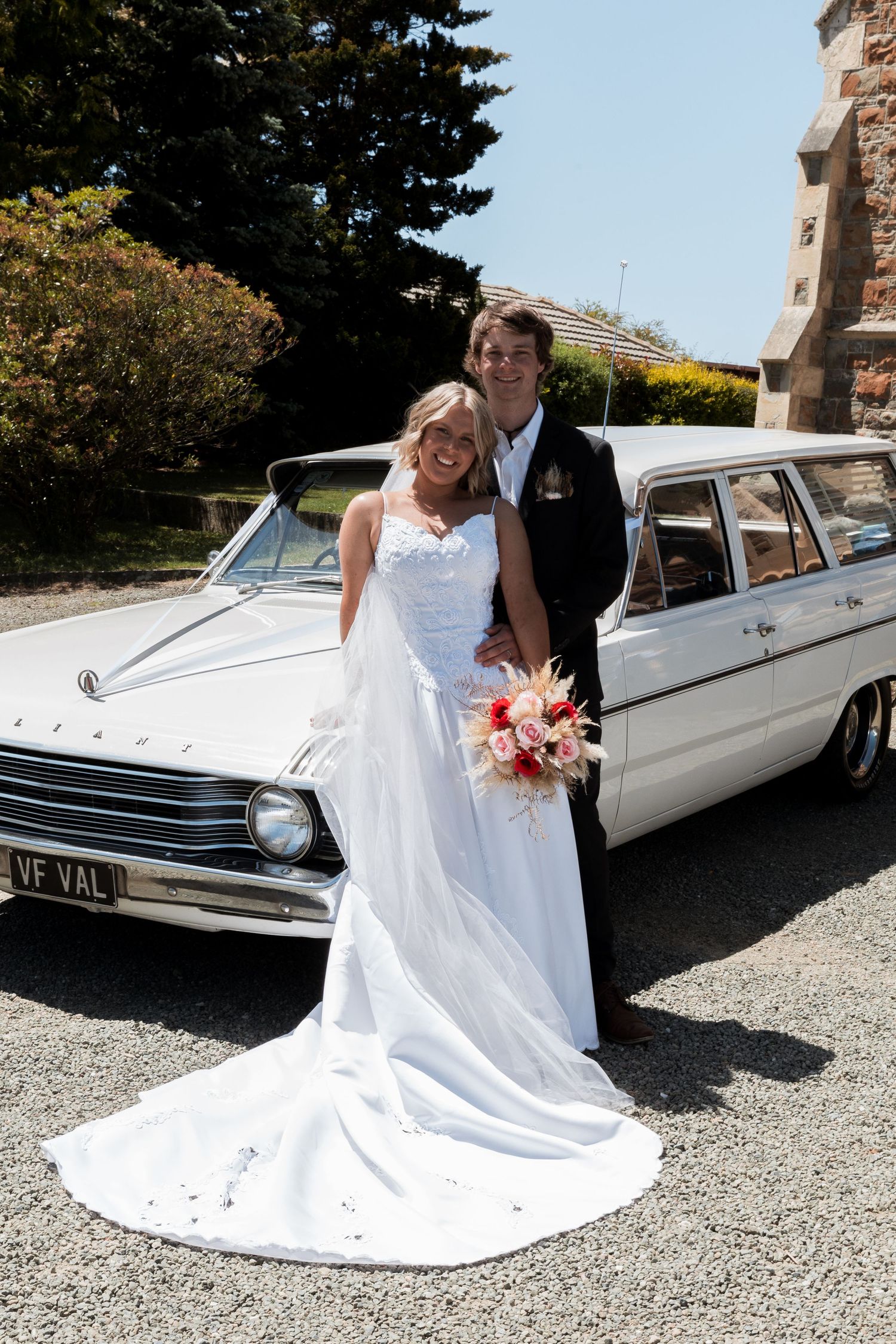Couple poses with classic white car on sunny wedding day.