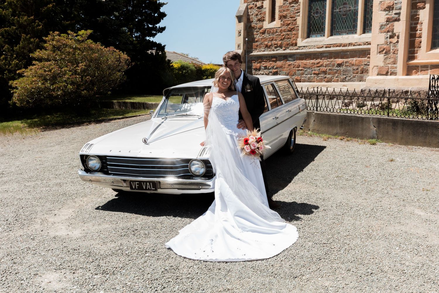 Classic white vintage limousine parked in front of stone church for wedding photography.