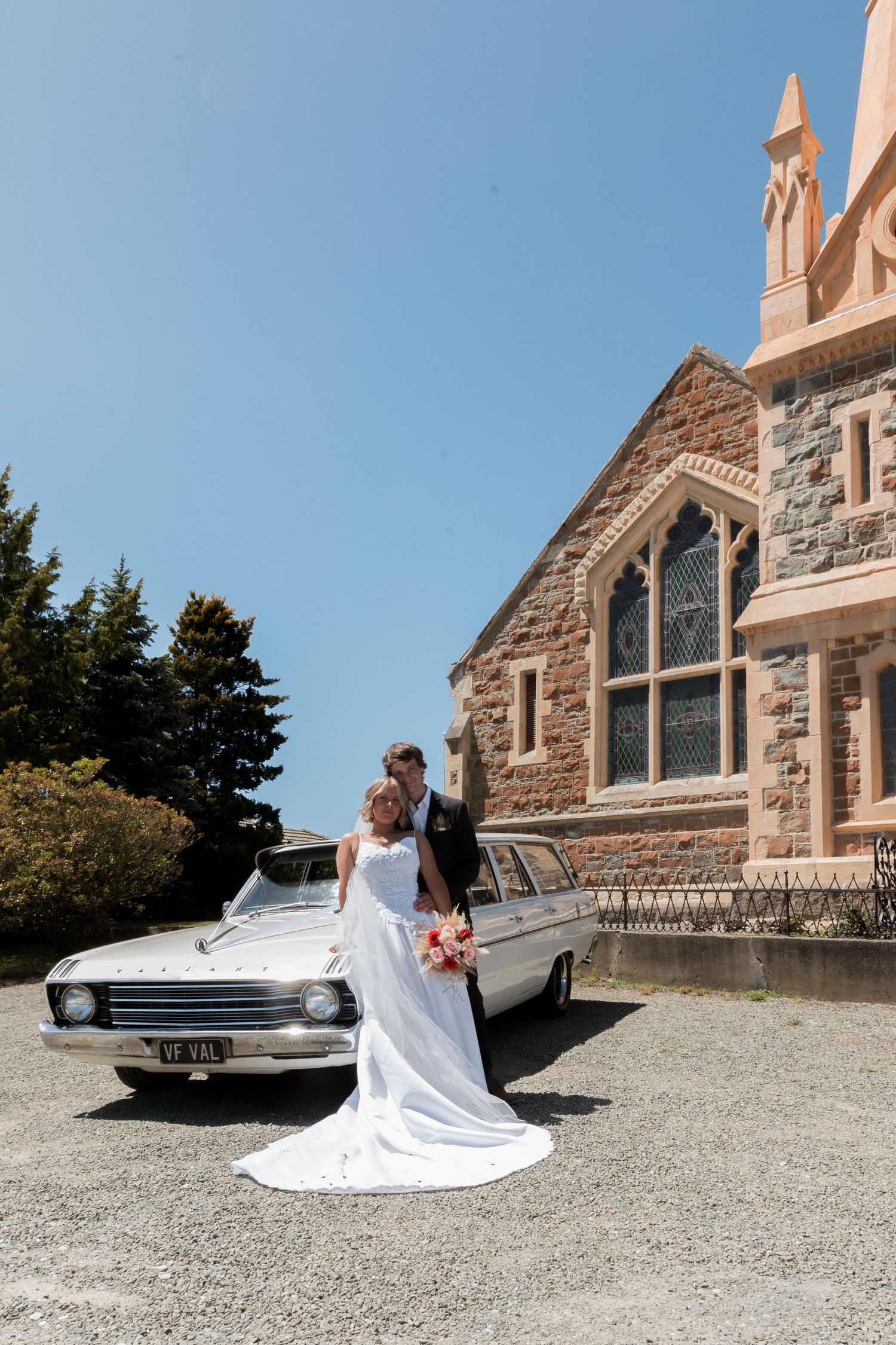 Elegant wedding scene with vintage white car against stone church architecture.