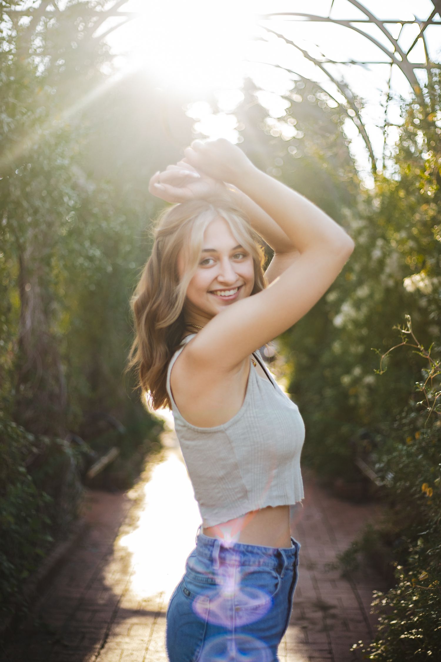 Senior portrait with hands on her head smiling at camera Captured at munsinger garden Park by Shania hirdler Photography