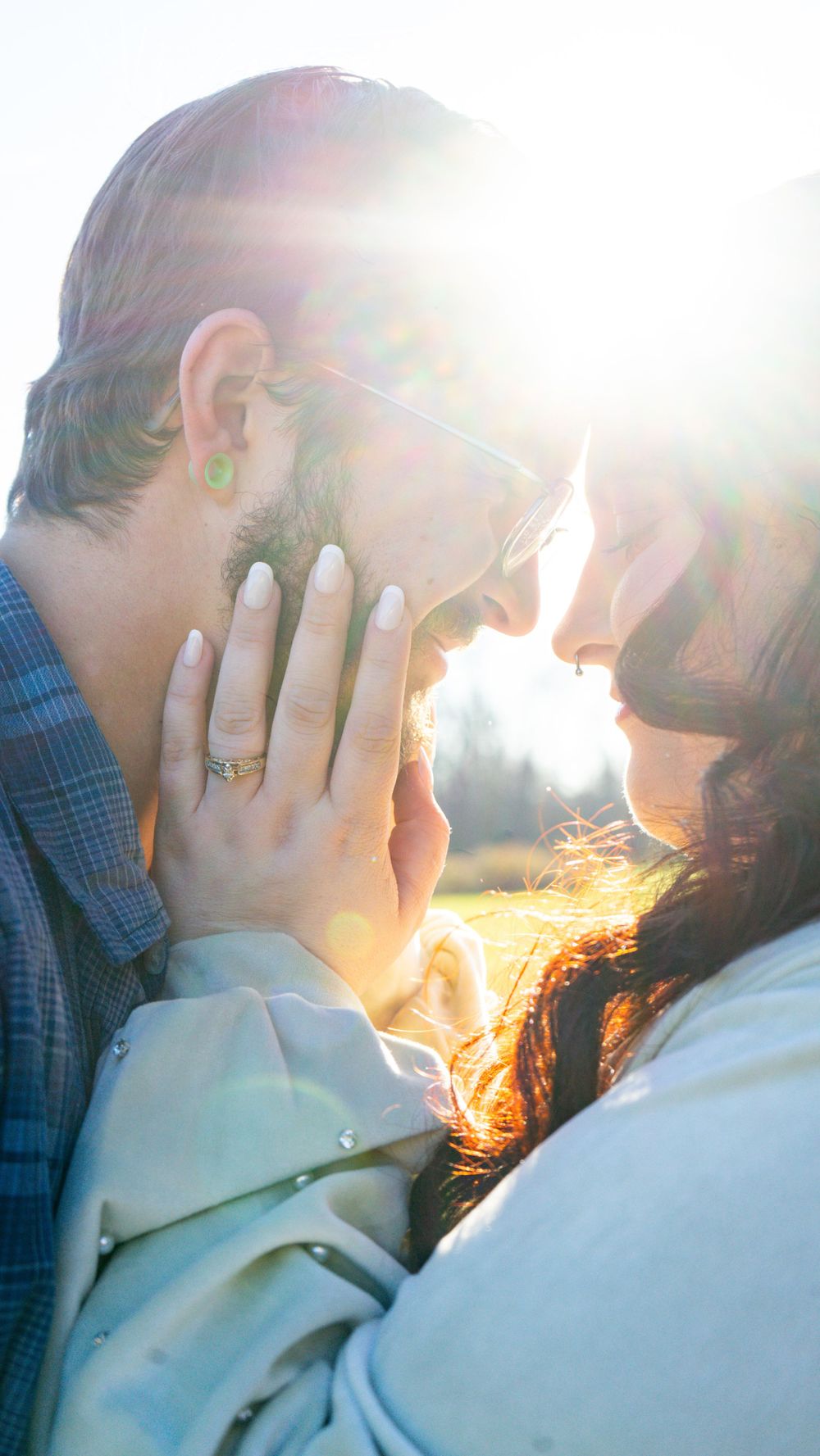 A couple shares an intimate moment in golden sunlight while showing off an engagement ring.