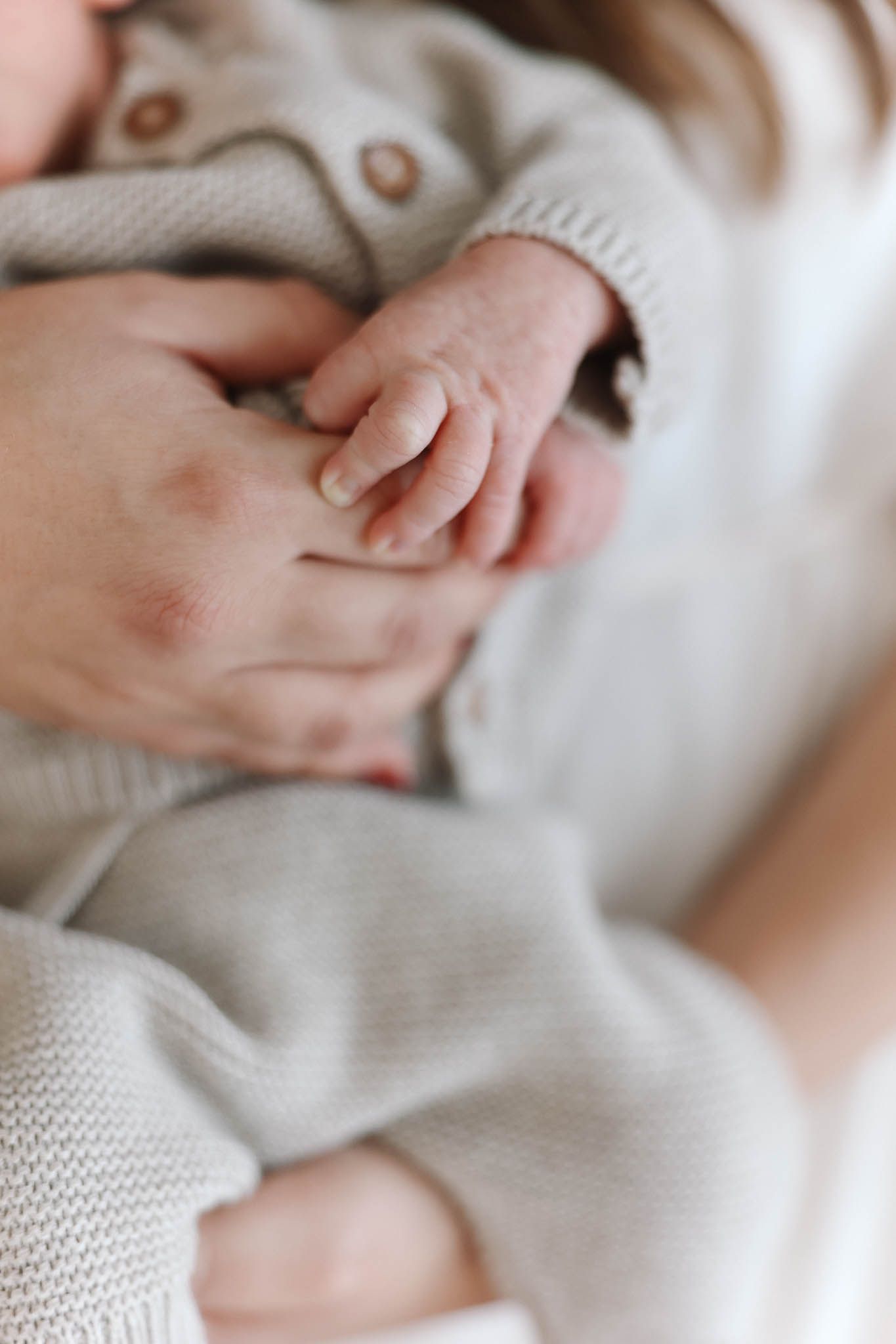 Close up of a tiny baby's hand grasping an adult's finger while wearing a soft gray knit sweater.