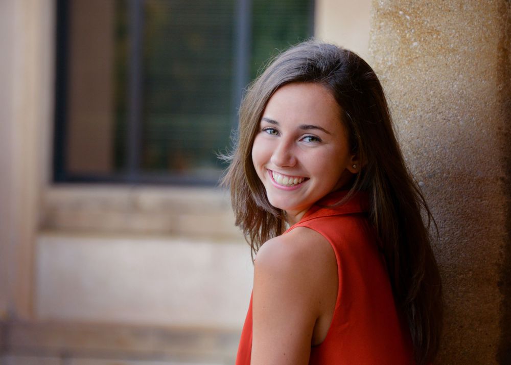 Portrait against textured wall wearing vibrant orange sleeveless top with natural lighting.
