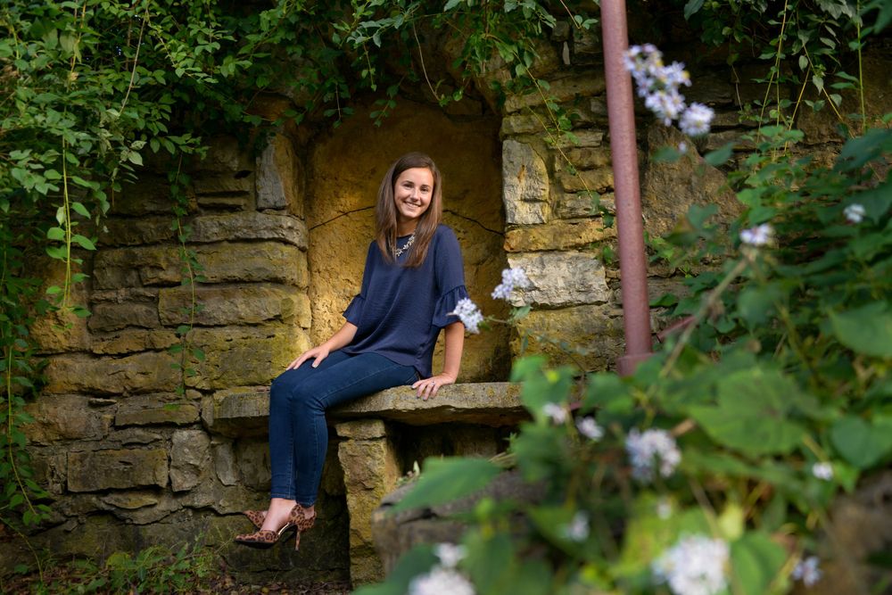 Person in navy outfit sitting in stone alcove surrounded by flowering vines.