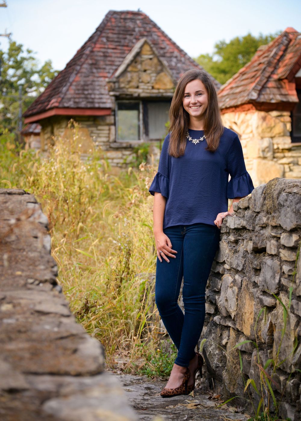 Professional photo against rustic stone wall and historic building backdrop featuring navy blue top and dark jeans.