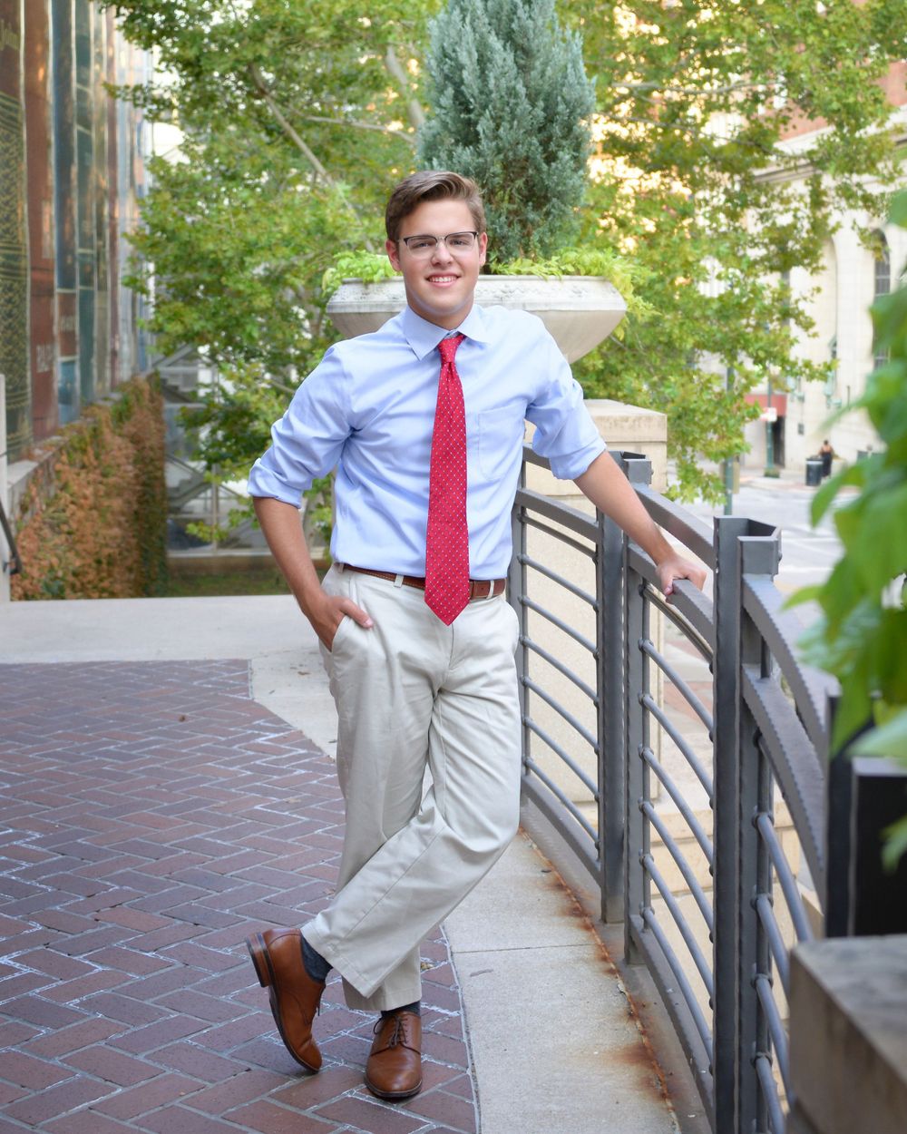 Professional outdoor portrait in business attire with red tie against urban landscaping.