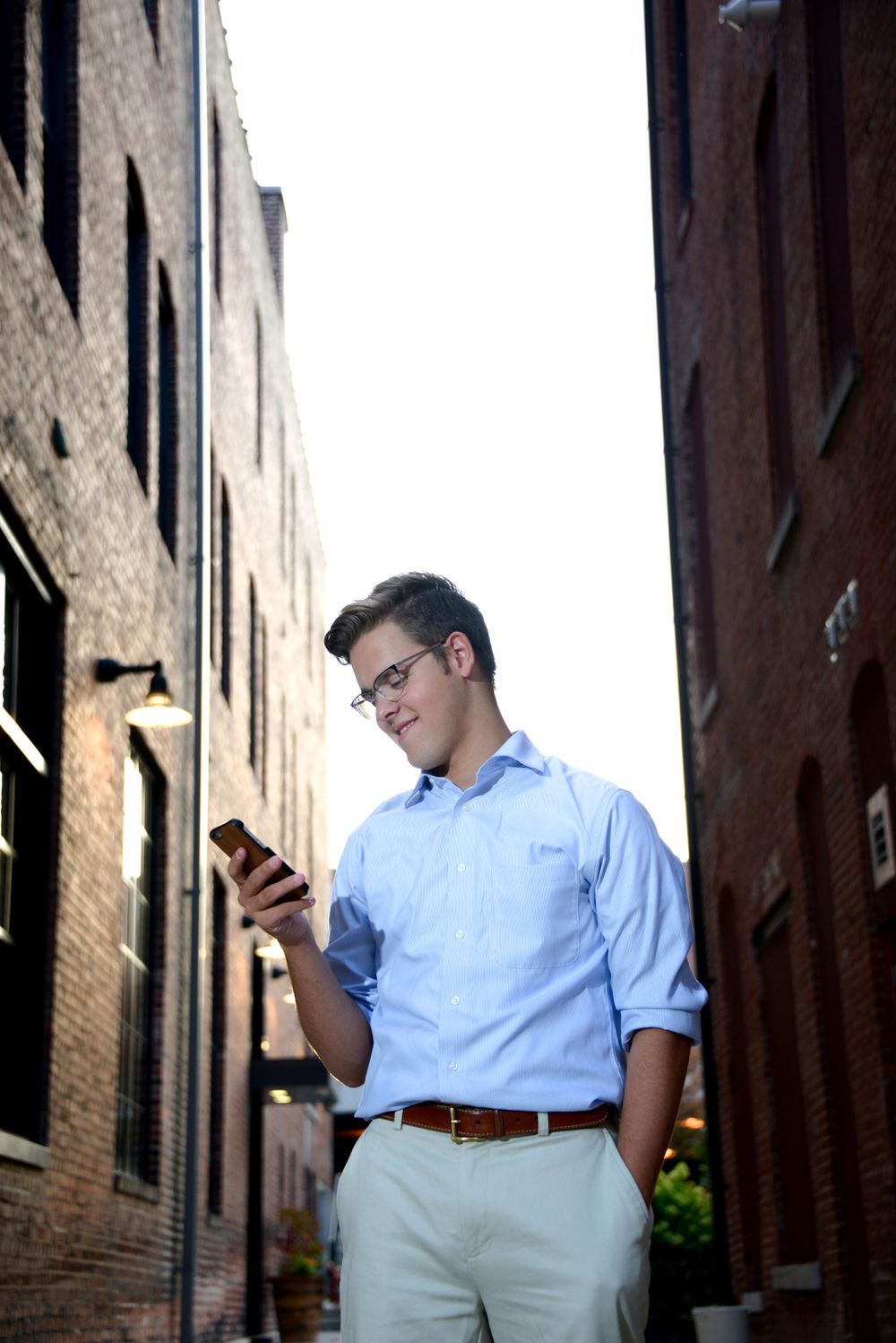 Professional checking smartphone while standing between brick buildings in urban alley.
