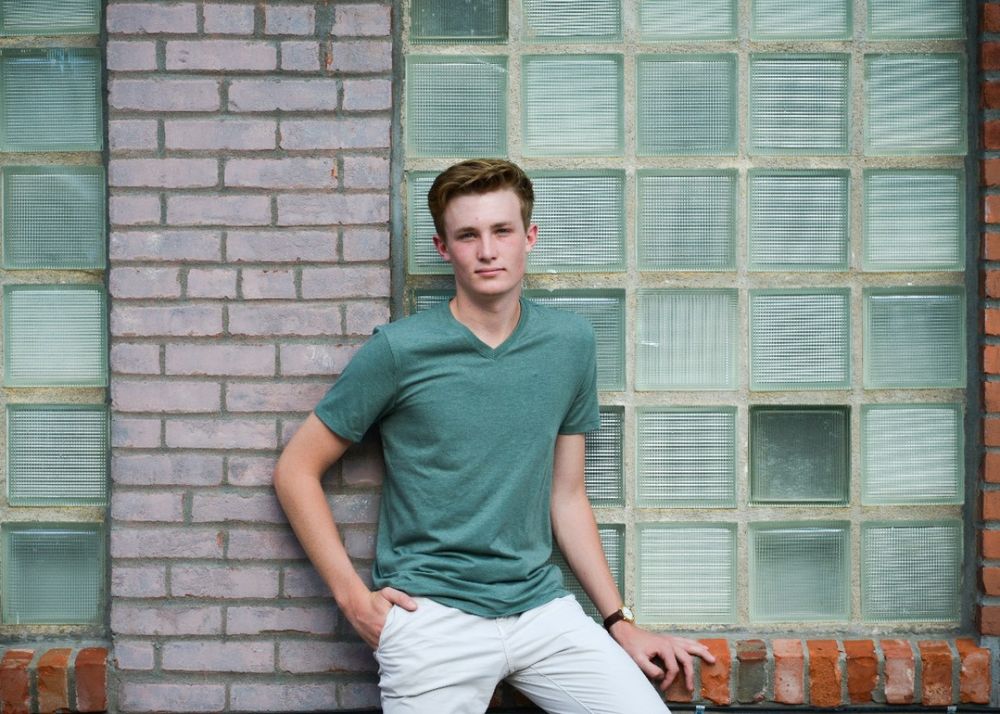 Casual portrait against glass block wall wearing sage green v-neck and light pants.