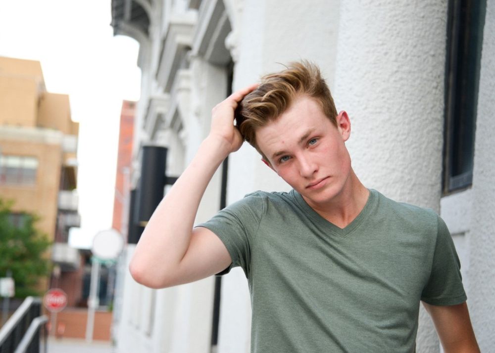 Urban portrait against white architectural column wearing casual green v-neck t-shirt.
