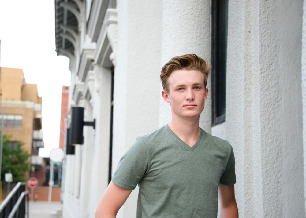 Casual outdoor portrait against white building exterior in olive green t-shirt.