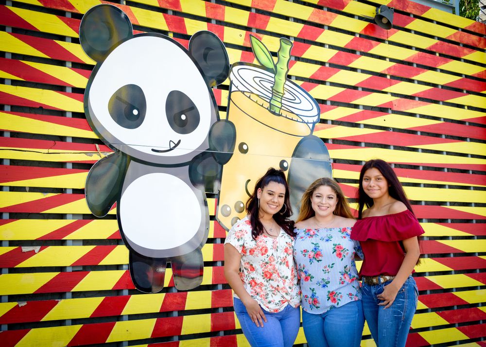 Group photo against colorful striped wall with cartoon panda and drink artwork.